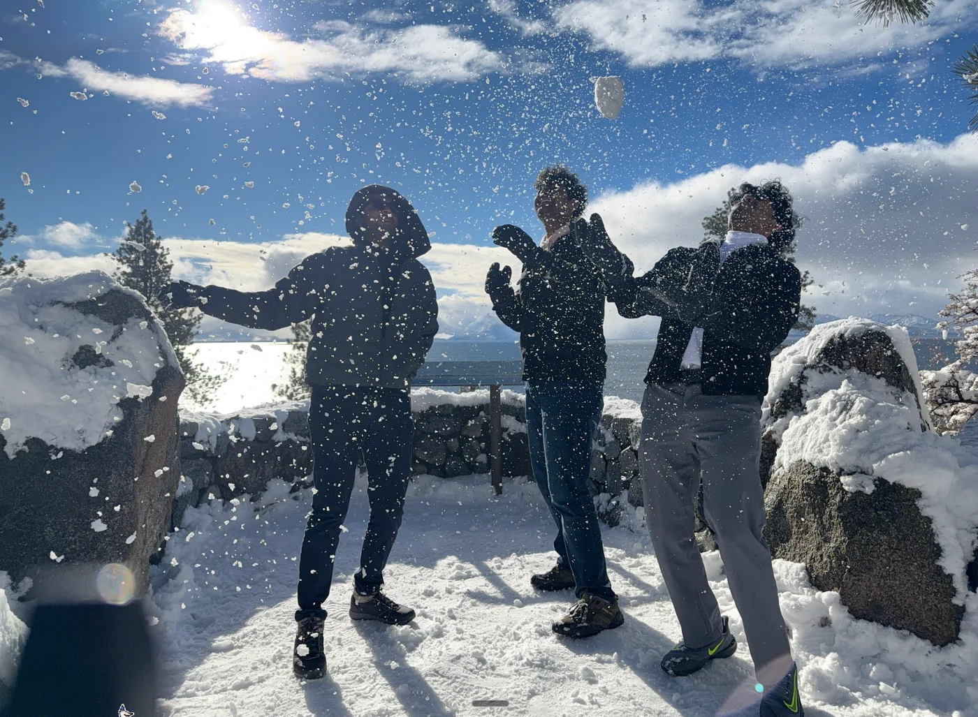 Three friends throwing snow into the air beside a mountain lake